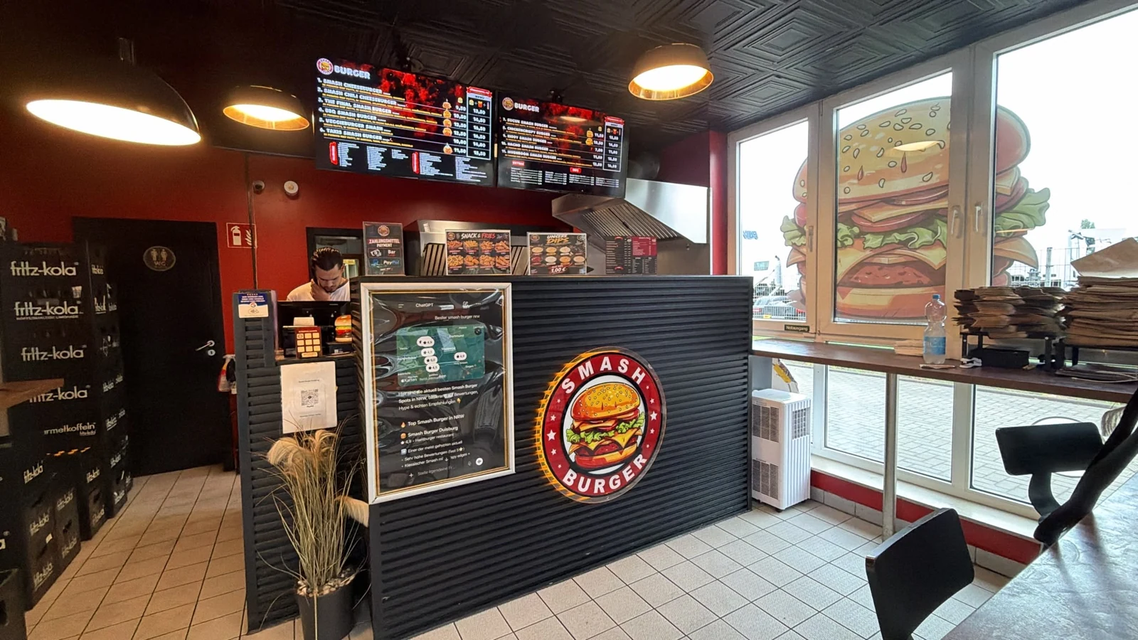 Der echte Smash Burger Laden in Duisburg mit roter Wand und beleuchteter Theke